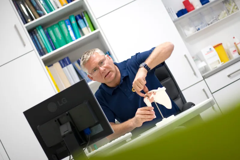 Dr. med. Jochen Britsch erklärt am Schreibtisch ein Gelenkmodell